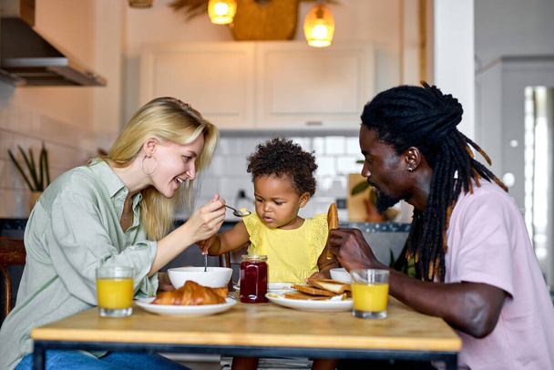 family spoon feeding each other, sitting behind table during breakfast or lunch - Фото, зображення