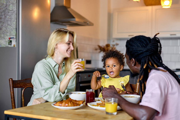Família jovem com criança tomando café da manhã em casa. Momentos familiares de estilo de vida feliz. - Foto, Imagem