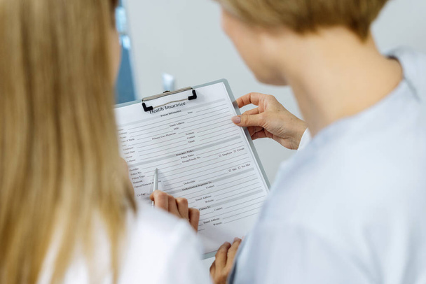Back view of professional female dentist standing in stomatology clinic, showing health insurance to patient, fill form, making notes in document, discussing a treatment plan - Photo, Image