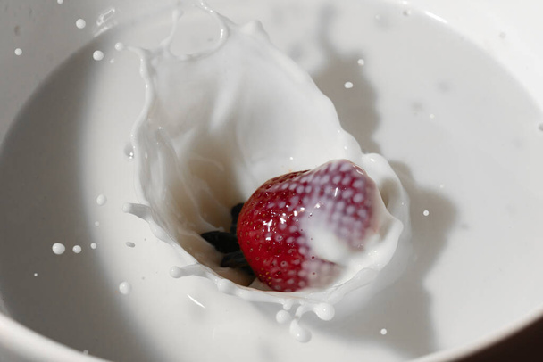 egy eper beleesik egy tejesbödönbe. a cseppek és az esés pillanata megfigyelhető. - Fotó, kép