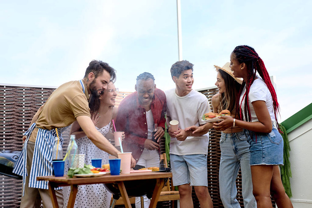 Young positive friends having barbecue party on the evening on house patio - 写真・画像
