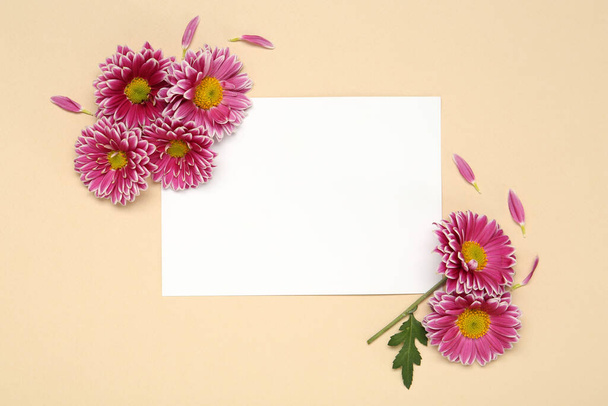 Beautiful chrysanthemums and blank card on beige background, flat lay. Space for text - Фото, изображение