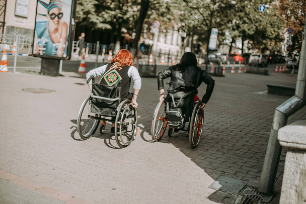 Twee meisjes in rolstoelen bij een reclamebanner met een lachend meisje. Vrouwen met speciale behoeften lopen rond Kiev in de buurt van Khreshchatyk en bewonderen de bezienswaardigheden. gelukkig meisje op een rolstoel met haar vriend - Foto, afbeelding