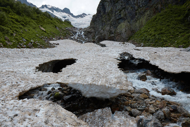 mountain landscape, melting snow, glacier and mountain stream, caves in ice - Photo, Image