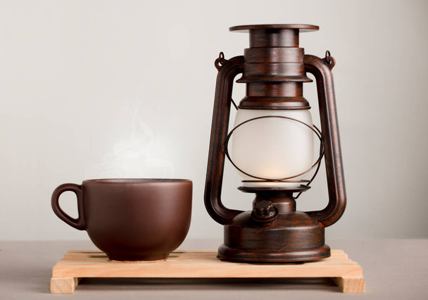 коричневая чашка кофе с горячим паром, на столе с солнечной лампой, серый фон - Фото, изображение