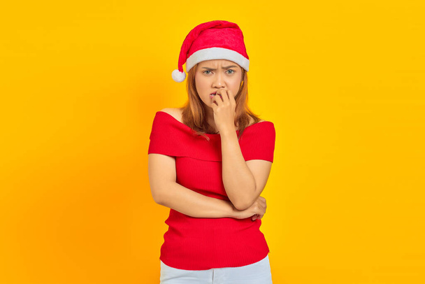Young Asian woman wearing Christmas hat looking stressed and nervous with hand on mouth biting nails - Фото, зображення