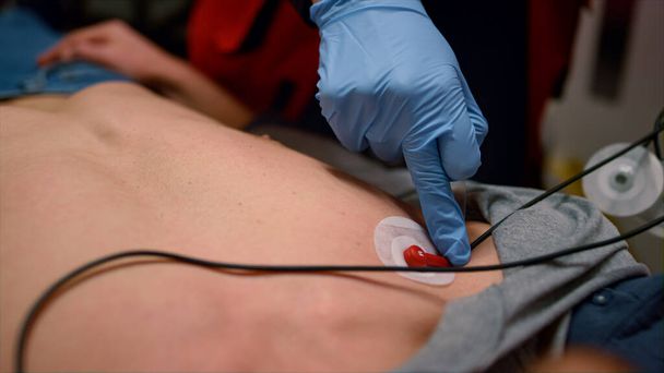 Mãos de médico de emergência aplicando sensores para medir o ECG do homem  - Foto, Imagem