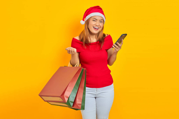 Lächelnde junge Asiatin mit Einkaufstaschen und Handy auf gelbem Hintergrund - Foto, Bild