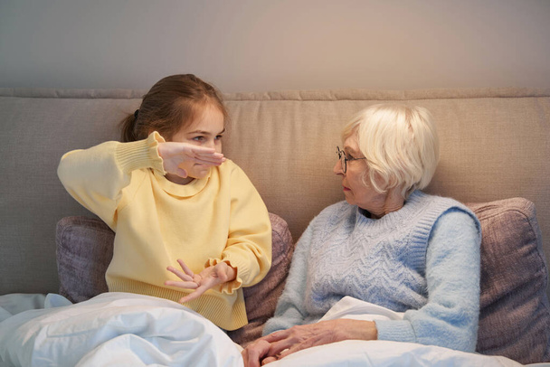 Serious grandmother playing charades with her granddaughter in bed - Φωτογραφία, εικόνα
