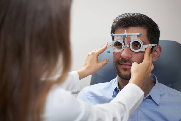 Optometrist adjusting trial frame on face of man - Foto, Imagen