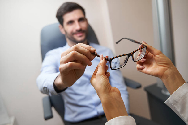 Ophthalmologist visitor taking glasses from doctor hand - Foto, afbeelding