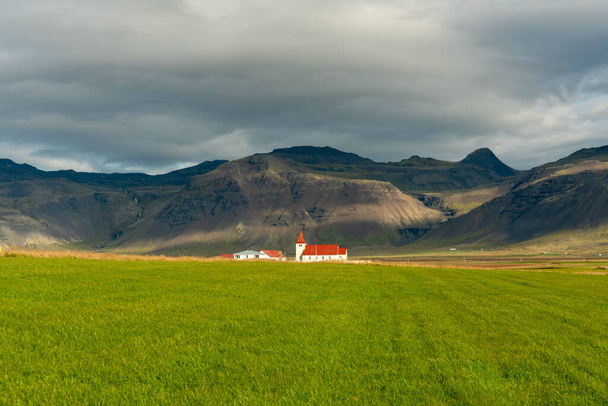 Weiße Kirche mit rotem Dach in Stadatstadur, Island. In einem grünen Tal am Fuße des Berges - Foto, Bild