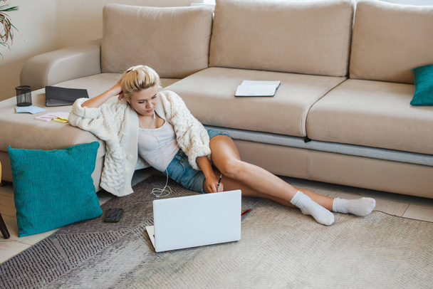 Caucasian woman using her laptop while lying on the floor and leaning from sofa. Studying from home. Distance education. - Foto, Imagem