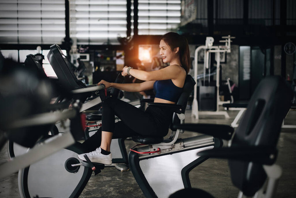 Feliz joven mujer sonriendo y haciendo ejercicio con el deporte en bicicleta de fitness en clase contra la interfaz de fitness. - Foto, Imagen