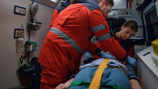 Rescue team of paramedics giving first aid help to victim in emergency car - 写真・画像