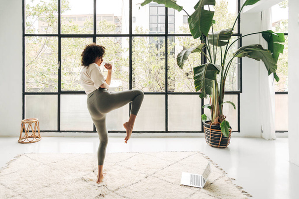 Young multiracial woman kicking leg up doing online fitness training at home living room. Copy space - Fotó, kép