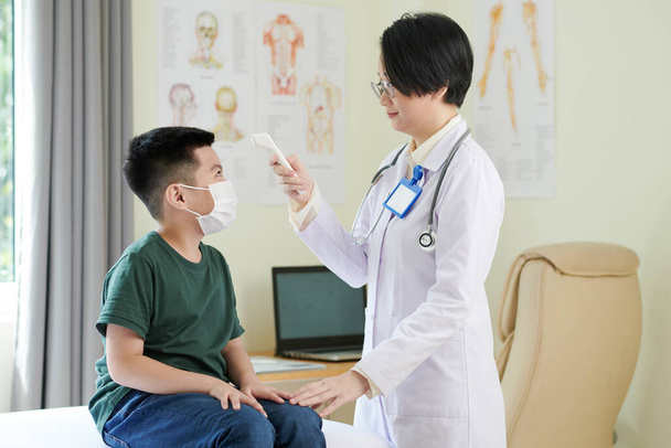 Doctor controleren lichaamstemperatuur van jongen - Foto, afbeelding