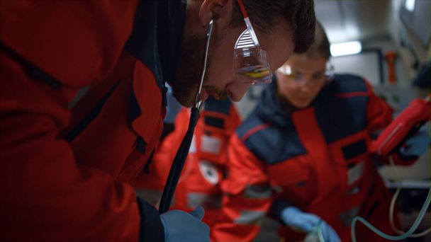 Paramedics team examining patient with stethoscope in emergency car - 写真・画像