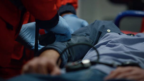 男はストレッチャーに横たわっていた。医療従事者が患者の腕に計量器を置く  - 写真・画像