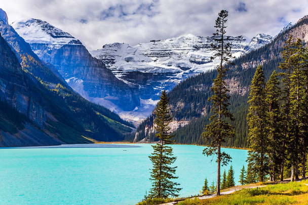 Beautiful sunny fine day. Glacial Lake Louise in Banff Park, Canadian Rockies. The lake with azure water is surrounded by mountains and forests. The concept of ecological, active and photo tourism - Foto, Imagem
