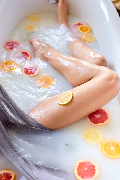 Top view On Female Legs, Attractive Woman Takes Milk Bath With Citrus Fruits - 写真・画像