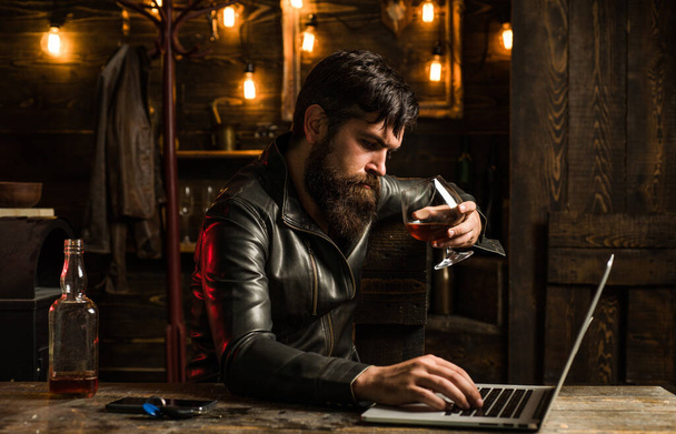 Businessman stressed with wiskey. Handsome man with a beard is sitting in a cafe with glass of whiskey and a laptop. - Foto, Bild