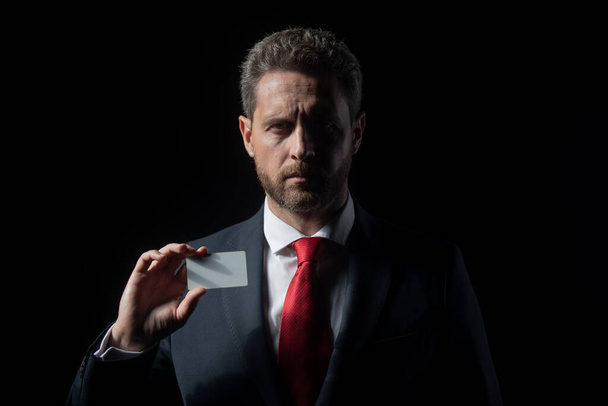 Studio portrait of serious businessman with credit card looking thoughtfully while standing at isolated dark background. Copy space. Face of business man. - Fotoğraf, Görsel