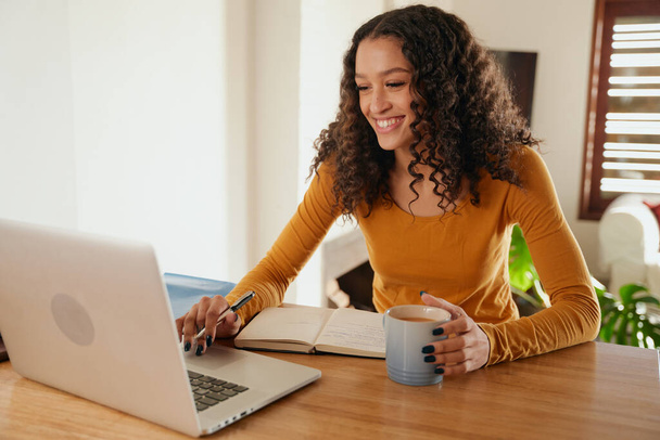 Афроамериканка-деловая женщина улыбается, работая из дома, печатая на ноутбуке  - Фото, изображение