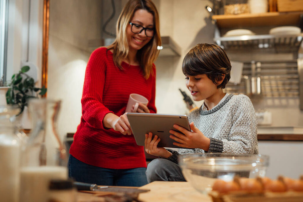 mother and son looking for recipes on digital tablet in kitchen - Фото, зображення