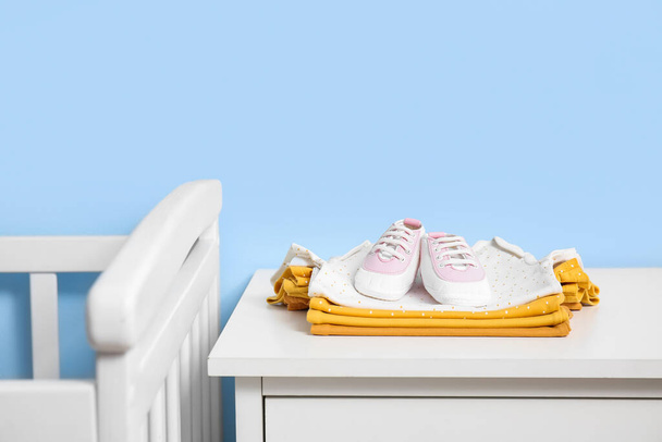 Pila de ropa de bebé y zapatos en el estante cerca de la pared azul - Foto, Imagen