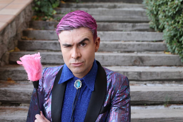 retrato de cerca del joven guapo en chaqueta púrpura con plumero rosa al aire libre - Foto, imagen