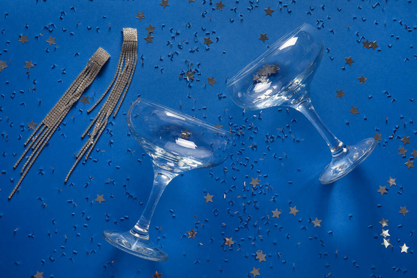 Kieliszki szampana, piękne kolczyki i konfetti na niebieskim tle - Zdjęcie, obraz