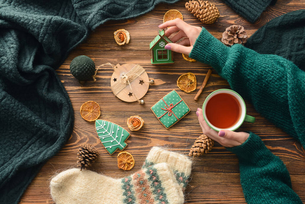 Жіночі руки з чашкою чаю, різдвяним одягом, печивом та прикрасами на дерев'яному фоні
 - Фото, зображення