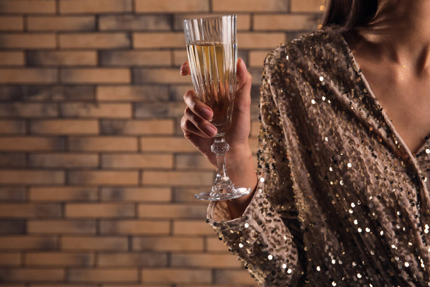 レンガの壁の近くにシャンパンのガラスを持っている女性,クローズアップ - 写真・画像