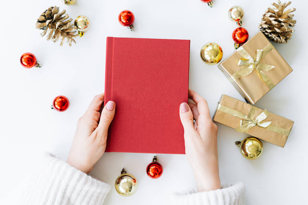um livro vermelho nas mãos de uma jovem no contexto de presentes e brinquedos de Natal. o conceito de Natal. Foto de alta qualidade - Foto, Imagem