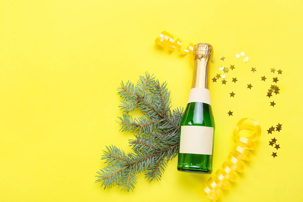 Σύνθεση με μπουκάλι σαμπάνια και χριστουγεννιάτικη διακόσμηση σε κίτρινο φόντο - Φωτογραφία, εικόνα