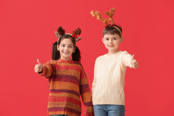 Смешные маленькие дети с оленьими рогами показывают большой палец вверх на цветном фоне - Фото, изображение
