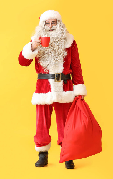Père Noël avec tasse de cacao chaud et sac sur fond jaune - Photo, image