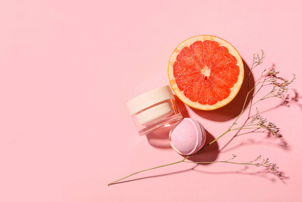 Bath bomb, jar of cosmetic product, grapefruit and dried flower on color background - Fotó, kép
