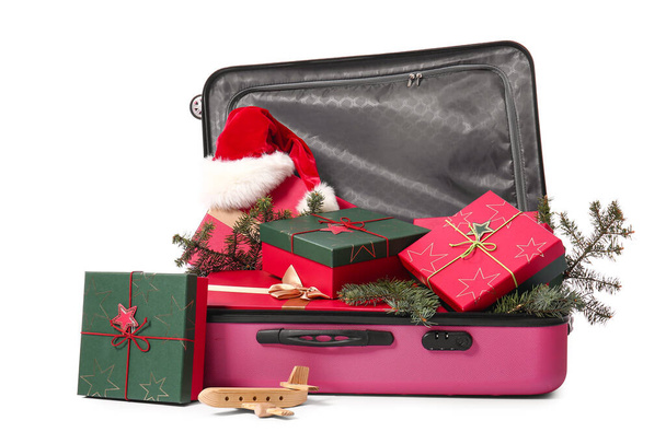 Suitcase with gift boxes, fir branches and Santa hat on white background. Christmas vacation concept - Photo, Image