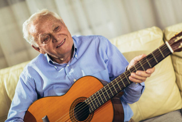Senior man playing guitar at home - Photo, image