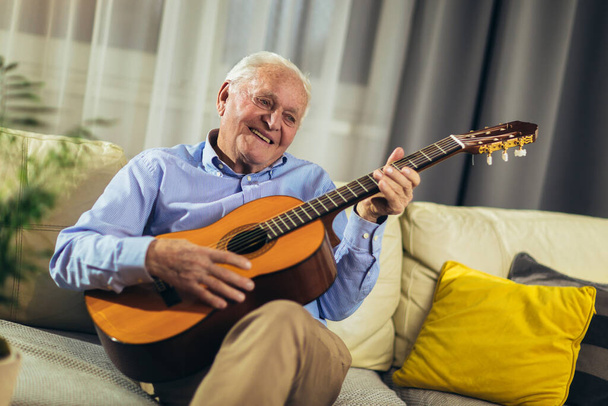 Senior man playing guitar at home - Фото, изображение