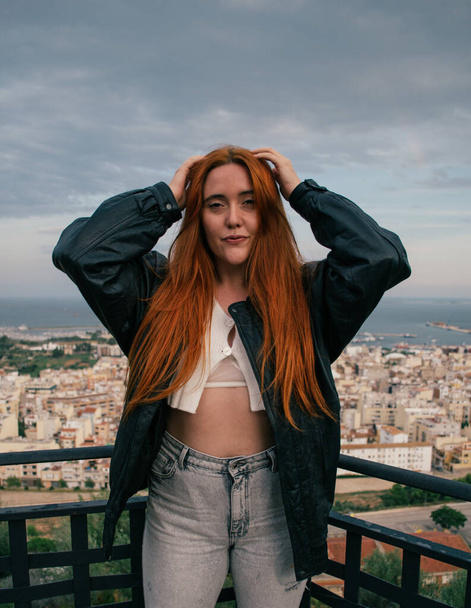 A red-haired Caucasian girl from Spain in black leather jacket with a white top and jeans - Fotó, kép