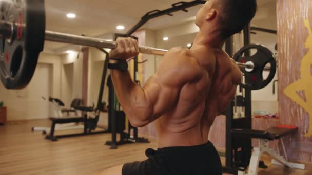 Nahaufnahme des Rückens eines jungen, muskulösen Mannes im Fitnessstudio, der auf einer Bank sitzend eine Langhantelpresse aus der Brust macht - Filmmaterial, Video