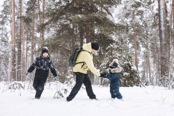 Otec a synové baví sněhové koule bojovat spolu v zimním lese. Šťastné děti si hrají venku ve sněhu. Vánoční prázdniny, novoroční rodinná dovolená. Bratři v teplém oblečení procházky v chladném dni - Fotografie, Obrázek