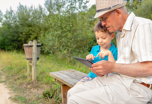 kleinkind en grootvader buitenshuis met behulp van een Tablet PC - Foto, afbeelding
