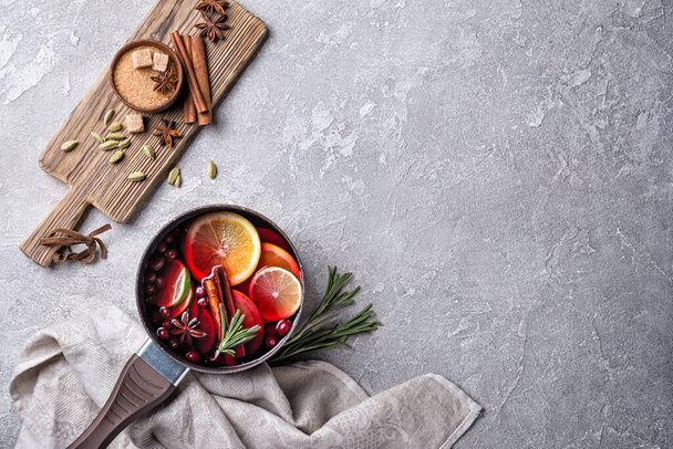 Autumn or christmas traditional drink with apples, oranges, cranberry, cinnamon, rosemary and other ingredients on grey concrete background - Photo, Image