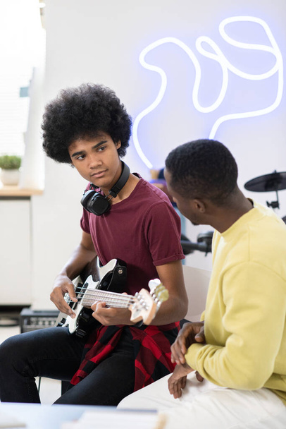 Усердный парень смотрит на своего учителя музыки во время игры на гитаре - Фото, изображение