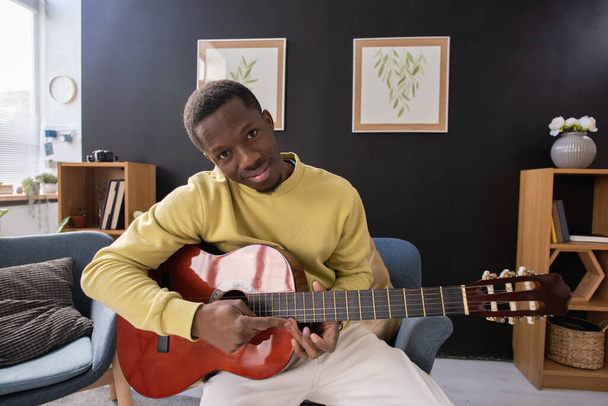 Nuori hymyilevä afrikkalainen mies akustinen kitara istuu kameran edessä - Valokuva, kuva