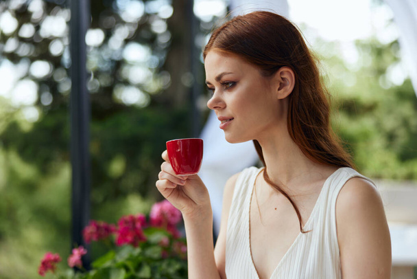Joven mujer con estilo en un vestido blanco bebe café al aire libre en un café inalterado - Foto, Imagen